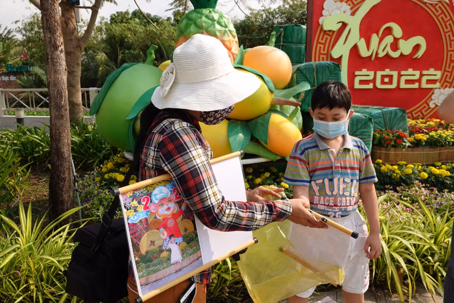  Một thợ chụp ảnh dạo giao ảnh lưu niệm cho khách nhí ở đường hoa Cần Thơ. Ảnh: Duy Tân