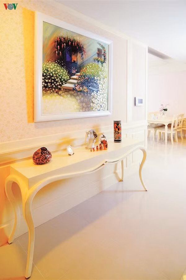 Chiếc bàn console ở bức tường hành lang đi vào phòng ngủ với nét duyên dáng cổ điển mà không rườm rà. Bức tranh hoa lá phía trên cũng thể hiện sự đồng nhất trong phong cách lãng mạn. 