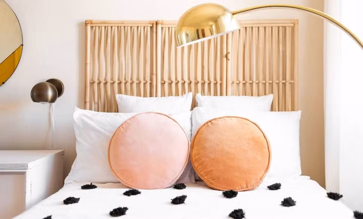 Giường ngủ trắng được trang trí cùng gối, họa tiết chấm bi và đèn ngủ cong tròn vàng đồng.