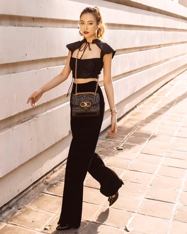 Hoàng Thùy Linh khai thác lợi thế eo thon với crop top khoét ngực, kết hợp quần ống rộng. Bộ cánh tuyền đen được nữ ca sỹ mix ăn ý với chiếc túi Gancio của Salvatore Ferragamo.