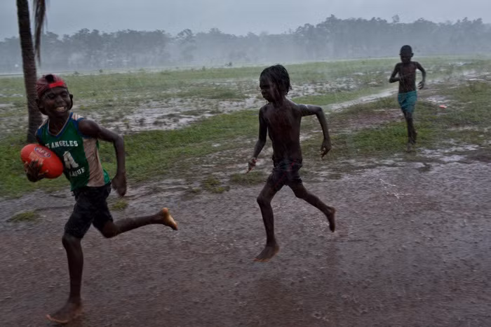 Một nhóm trẻ em chơi môn bóng đá kiểu Úc trong mưa tại khu dân cư Pirlangimpi, đảo Melville - Ảnh: DAVID MAURICE SMITH, OCULI/NG