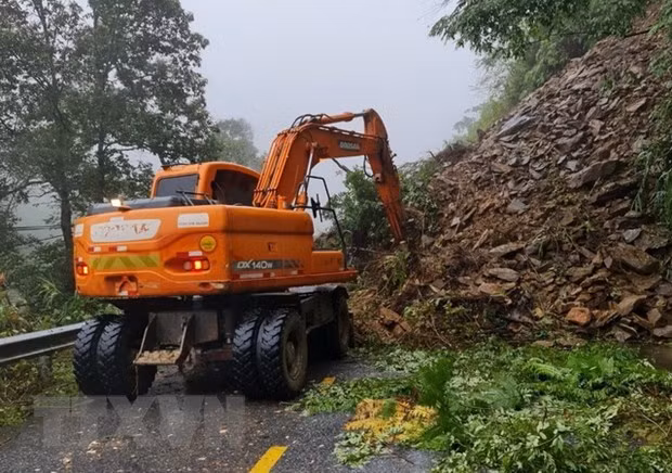 Lực lượng chức năng triển khai phương tiện máy móc tiến hành khắc phục sạt lở đất gây ách tắc giao thông. (Ảnh: TTXVN phát)