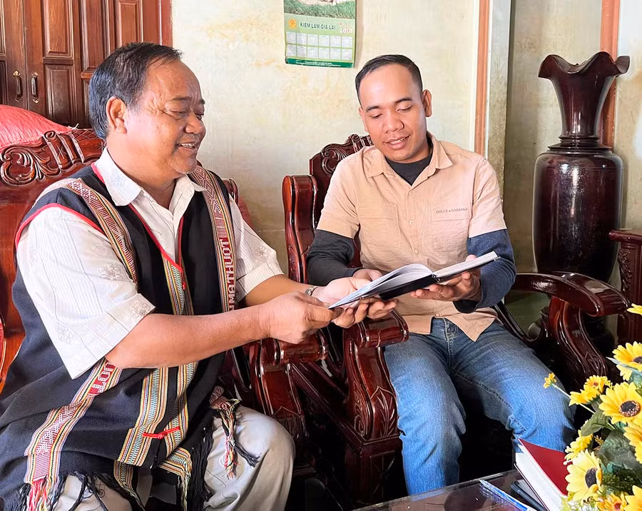  Ông Siu Bi Ai (bìa trái) trao đổi với phóng viên về xây dựng nông thôn mới tại địa phương. Ảnh: R'Ô HOK