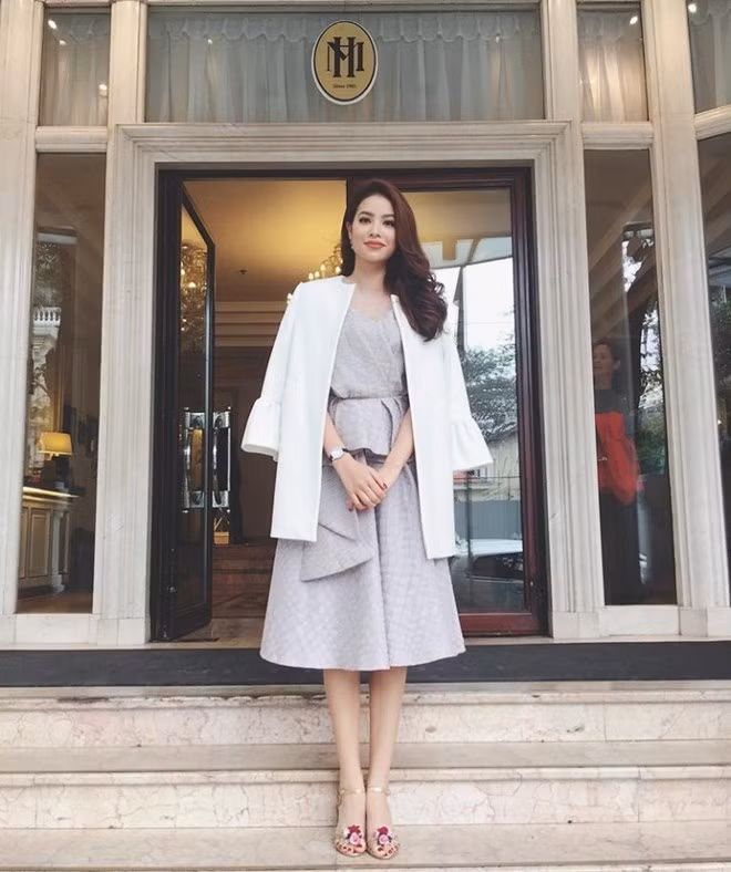Phạm Hương hóa nàng tiểu thư kiêu kỳ trong bộ đầm màu phấn trang nhã, blazer trắng khoác hờ trên vai để nhấn nhá vẻ ngoài sang trọng. Sandals đính hoa là phụ kiện ấn tượng khiến tổng thể trang phục thêm lôi cuốn, bắt mắt.