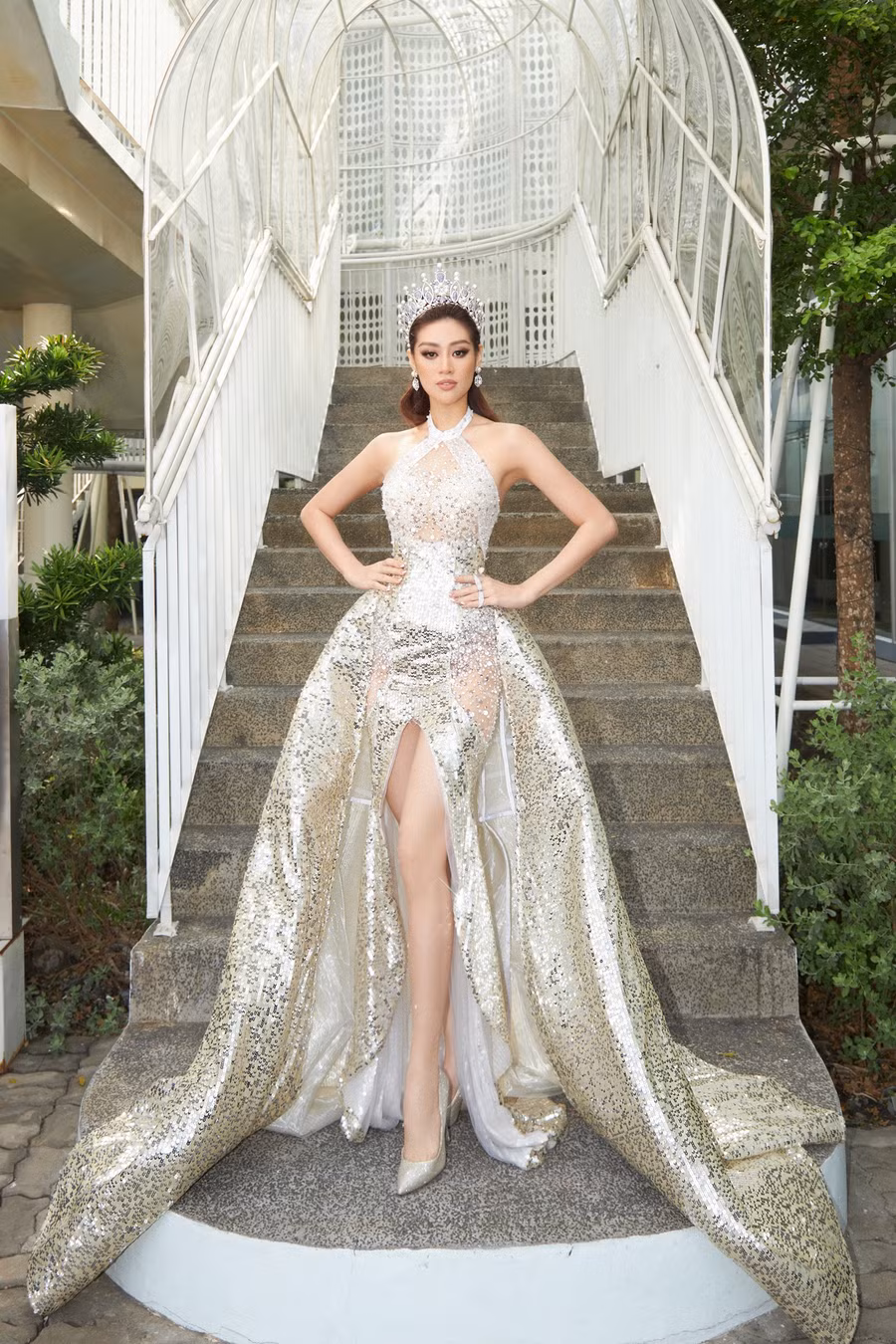 Mẫu váy kết hợp 2 trong 1 - bên trong là kiểu đầm đuôi cá ôm sát cơ thể và xẻ tà cao kết hợp phần tùng váy bồng bềnh dài quét đất giúp bước đi thêm thướt tha. Chất liệu lấp lánh từ bề mặt vải được đính kết xen kẽ các phần xuyên thấu giúp 